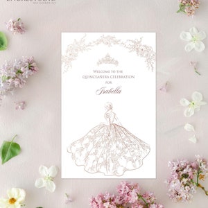 Puede incluir: Una tarjeta blanca con un diseño floral dorado y una corona. El texto dice "Bienvenido a la celebración de Quinceañera para Isabella". Un contorno dorado de una mujer con un vestido de bola está debajo del texto.