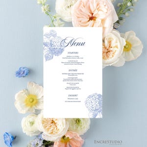 May include: A wedding menu card with floral illustrations and text, surrounded by an arrangement of white, peach, and blue flowers on a light blue background. The menu includes starters, entrees, and dessert options.
