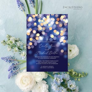 May include: A rectangular wedding invitation card with a dark blue background featuring a bokeh light effect of gold and white circles. The text reads: Together with their parents, Emily Anne and Michael Dillon, request the honour of your presence at their wedding ceremony, Saturday, the twenty-third of July, two thousand twenty-eight, at four o'clock in the afternoon, St. Patrick's Church, San Diego, California.