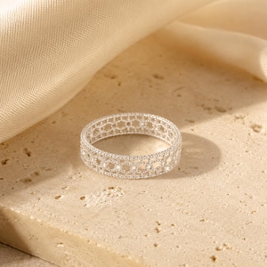 May include: A silver-toned ring featuring an intricate, openwork lattice pattern that resembles delicate lace. The band has a consistent width throughout, with a textured, metallic finish that catches the light across its repeating geometric design.