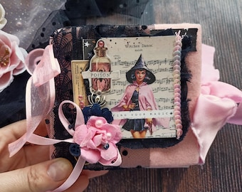 May include: A small, square, pink felt-covered book with black lace trim. The cover features a collage with a witch illustration, a potion bottle labeled POISON, musical notes, and the text Witches Dance and FIND YOUR MAGIC, accented with a pink fabric flower.