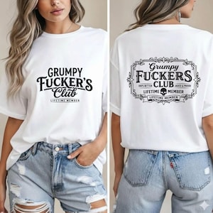 Puede incluir: Una camiseta blanca con texto negro en la parte delantera que dice Grumpy Fucker's Club Lifetime Member. La parte posterior de la camiseta muestra un marco rectangular decorativo que contiene el texto Grumpy Fucker's Club, 100% Bitter, Jaded & Proud, y Lifetime Member con un icono de calavera.
