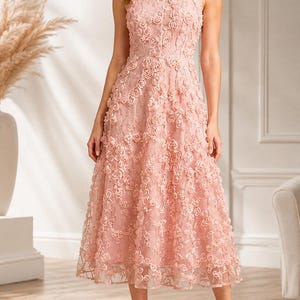 May include: A sleeveless midi dress in a soft blush pink hue, featuring a round neckline and a fitted bodice. The entire garment is adorned with intricate, three-dimensional floral appliqués that create a textured, layered rose pattern.