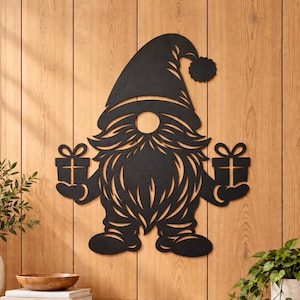 May include: A black silhouette wall art piece depicting a gnome wearing a pointed hat with a pom-pom, featuring a long beard and holding a gift box in each hand. The text at the bottom reads: Instant Download | DXF, SVG, EPS & PNG.