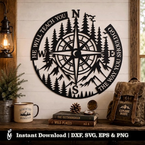 May include: A circular black metal wall art piece featuring a compass rose design, silhouettes of pine trees and mountains, and the text "HE WILL TEACH YOU THE WAY YOU SHOULD GO". The design includes cardinal directions N, S, E, and W.