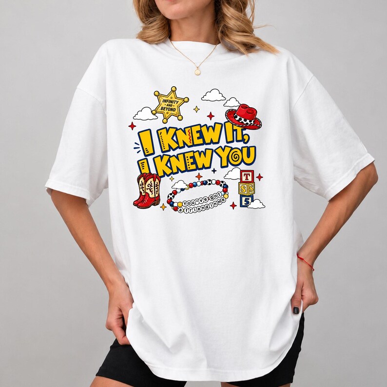 May include: A white t-shirt featuring a graphic print with the text I KNEW IT, I KNEW YOU. The design includes a yellow sheriff badge, a red cowboy hat, red cowboy boots, a colorful beaded bracelet with text, and three stacked alphabet blocks.