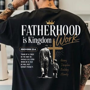 May include: A black t-shirt featuring white and gold text that reads FATHERHOOD is Kingdom Work. It includes a graphic of a person and a child walking toward a cross, the text PROVERB 22:6, and the words Raising, Discipline, Building, Eternity.