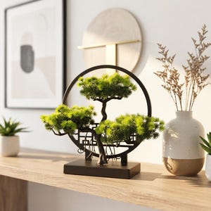 May include: A decorative artificial bonsai tree featuring vibrant green needle-like foliage and a dark brown trunk, mounted within a circular black frame with a rectangular base. The structure includes a geometric lattice pattern at the bottom.