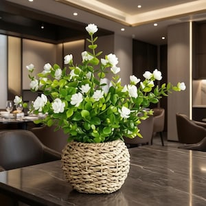 May include: A decorative plant with small white flowers and vibrant green leaves arranged in a rounded, woven light brown basket. The plant features multiple stems extending upwards, creating a full, bushy appearance in a round container.