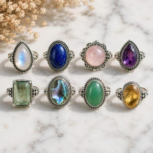 Puede incluir: Ocho anillos de tono plateado dispuestos en dos filas, cada uno con una piedra preciosa única. Las piedras incluyen piedra de luna, lapislázuli, cuarzo rosa, amatista, cuarzo verde, concha de abulón, aventurina verde y citrino en bandas metálicas.