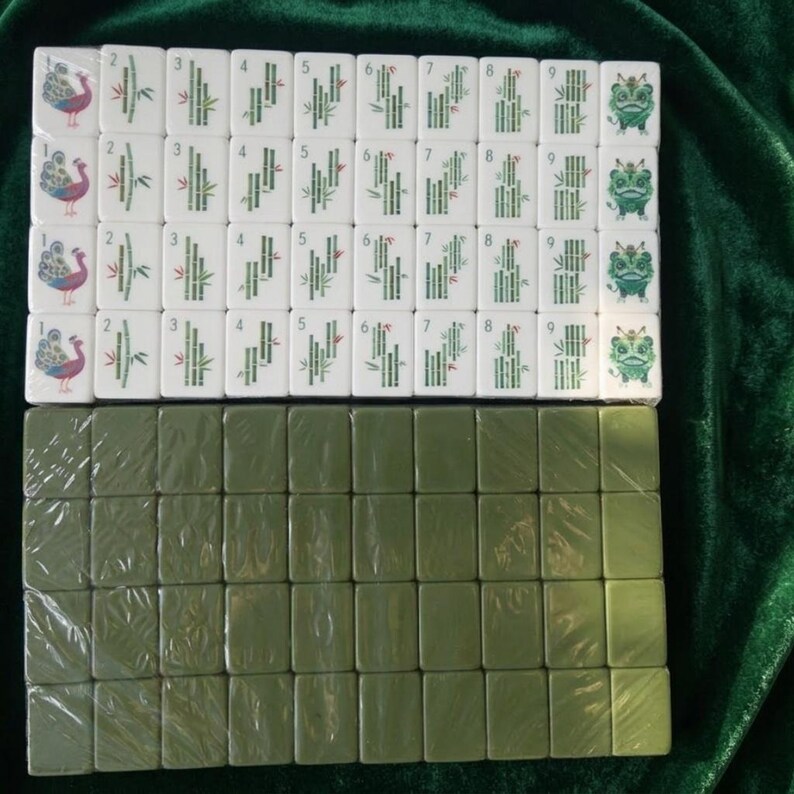 Mahjong tile set displayed on green velvet fabric showing white bamboo suit tiles numbered 1 to 9 with peacock and lion designs plus olive green back tiles arranged in rows traditional Chinese mahjong game set with colorful illustrated symbols suitable for family game nights and collectors