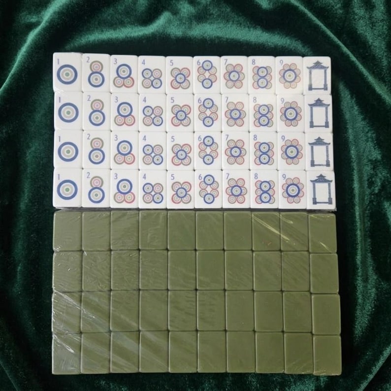 Mahjong tile set displayed on green velvet fabric showing white tiles with colorful circle suit symbols numbered 1 to 9 arranged in four rows alongside olive green back-facing tiles, complete traditional Chinese mahjong game set with numbered dot tiles and pagoda design, suitable for family game nights and tournaments