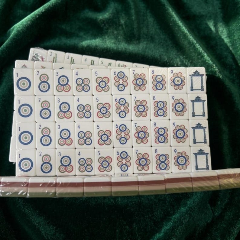 Mahjong tile set with circle suit tiles numbered 1 to 9 arranged in neat rows, white plastic tiles featuring colorful concentric circle designs and pagoda honor tiles, displayed on green velvet fabric, traditional Chinese mahjong game complete set ideal for family game nights and strategy play