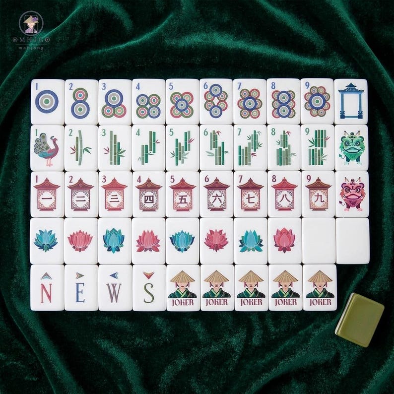 American mahjong tile set displayed on green velvet showing complete suit layout including dots bamboo and characters with lotus flower winds joker tiles featuring elegant Asian-inspired illustrations of pagodas peacock and lion dance designs on white tiles