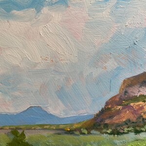 Original New Mexico landscape oil painting detail from “Finding My Way to Pedernal” by Santa Fe artist Dawn Chandler, showing Pedernal’s iconic flat-topped silhouette in cool blue beyond open green fields and low mesa slopes, with layered pastel clouds and subtle atmospheric perspective conveying the spacious light of O’Keeffe country.