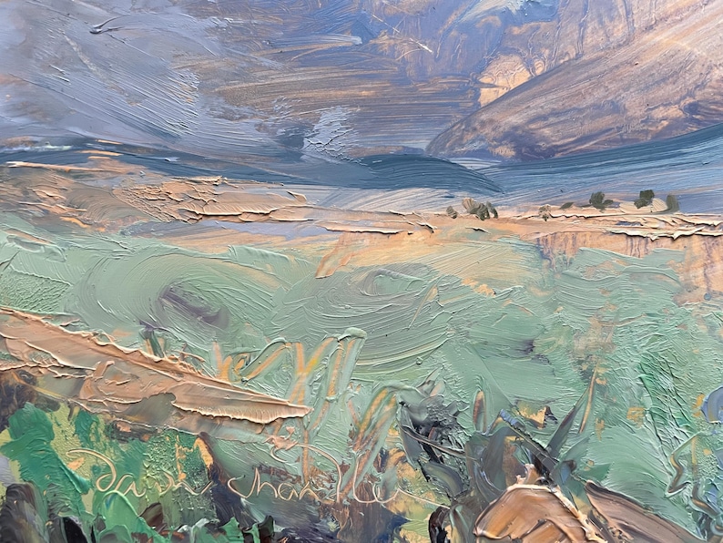 Close-up detail of original New Mexico landscape painting Spring Morning Over the Taos Mountains by Santa Fe artist Dawn Chandler, focusing on the richly textured foreground where thick impasto strokes describe mint and sage green spring grasses, ochre earth, and hints of distant fields beneath shadowed blue foothills, revealing the physical brush marks, palette-knife ridges, and the artist’s signature inscribed into the wet paint.