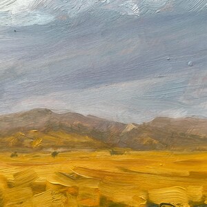 Soft morning haze settles over golden meadows and distant New Mexico hills in October Morning Along Miami Lane by Santa Fe artist Dawn Chandler. The warm ochres and umbers evoke early sunlight glancing off the slopes of Philmont just after sunrise.