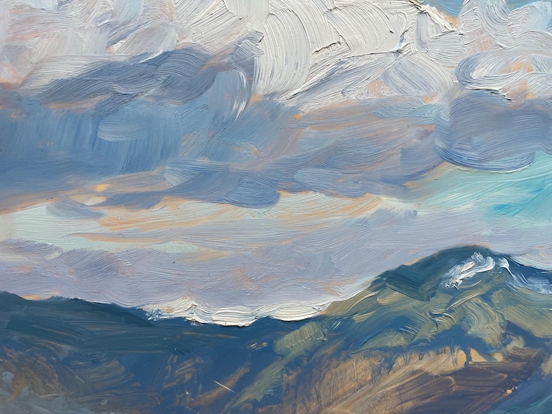 Close-up section of original New Mexico landscape painting Spring Morning Over the Taos Mountains by Santa Fe artist Dawn Chandler, focusing on the dynamic sky where broad, gestural strokes of white, lilac, and slate-gray clouds move across pale turquoise and soft blue atmosphere over the mountain ridge, capturing the shifting spring weather and expressive brushwork in the oil paint.