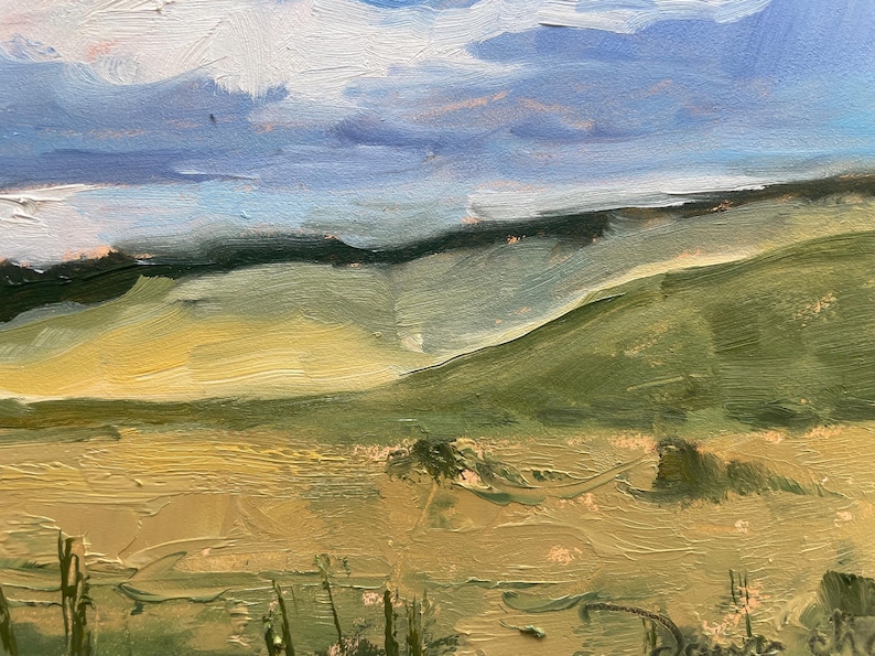 Close‑up view of Dawn Chandler’s original New Mexico landscape painting Under a High Country August Sky, highlighting the rolling green hillside and golden high‑country field with thick, directional brushstrokes, scattered sagebrush forms, and soft shadows receding toward a dark tree line under a layered sky of blue, lavender, and creamy clouds.