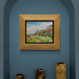 Original New Mexico landscape oil painting “Finding My Way to Pedernal” by Santa Fe artist Dawn Chandler, framed in a textured gold frame and displayed in a blue arched niche with three rustic wooden candleholders below, demonstrating how this luminous Abiquiu mesa and Pedernal view becomes a focal point in Southwestern or contemporary decor.