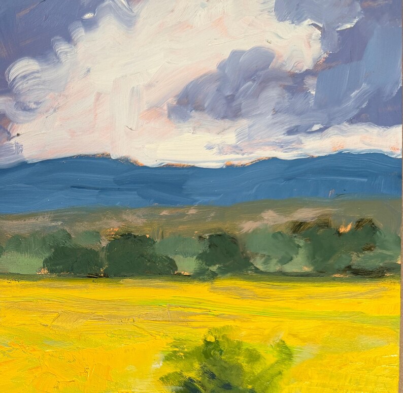 Panoramic detail of Dawn Chandler’s original New Mexico landscape painting, showing a wide band of Abiquiu’s yellow summer field, dark green tree line, distant blue mountains, and soft swirling clouds, with visible brushwork conveying the energy and atmosphere of a late-summer afternoon in northern New Mexico.