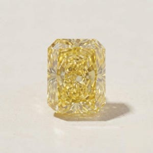 May include: A radiant-cut yellow gemstone with a rectangular shape and numerous facets that create a complex, symmetrical pattern of light reflection. The stone displays a vibrant, saturated yellow hue throughout its entire crystalline structure.