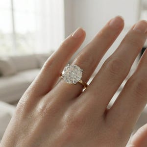 May include: A solitaire ring featuring a large, round, brilliant-cut clear gemstone set in a four-prong setting. The band is crafted from polished yellow gold, providing a warm contrast to the bright, faceted white stone held securely at the center.