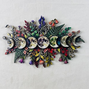 Pu&ograve; includere: Una decorazione da parete che presenta una disposizione orizzontale delle fasi lunari circondate da colorate illustrazioni botaniche, tra cui felci, varie foglie e piccoli fiori nelle tonalit&agrave; del viola, rosso, arancione, giallo e verde.