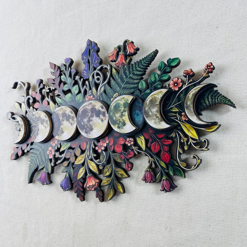 Pu&ograve; includere: Una decorazione da parete con una disposizione orizzontale delle fasi lunari, dalla falce alla luna piena, circondata da illustrazioni dettagliate di felci, foglie e vari fiori colorati nelle tonalit&agrave; del rosso, viola, giallo e verde.