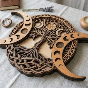 May include: A layered wooden wall art piece featuring a central tree design surrounded by intricate Celtic knotwork and two crescent moon shapes. The circular structure displays various moon phases carved into the wood, showcasing natural light and dark brown wood tones with detailed cutouts.
