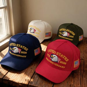 Puede incluir: Cuatro gorras de béisbol en azul marino, crema, verde oliva y rojo. Cada una presenta el texto bordado UNITED STATES 1776 2026 250TH ANNIVERSARY, un gráfico de águila calva y un pequeño parche de la bandera estadounidense en el panel lateral.