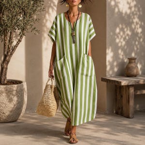 May include: A loose-fitting midi dress featuring vertical green and white stripes, short sleeves, a round neckline with a central slit, and two large front patch pockets. The dress is paired with a woven straw tote bag and a long pendant necklace.