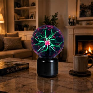 May include: A spherical plasma lamp with a black cylindrical base, emitting vibrant green and purple electrical filaments that radiate from a central glowing pink electrode, creating a dynamic light display on a polished stone surface.