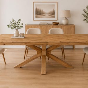 May include: A rectangular wooden dining table with a herringbone pattern tabletop and a central X-shaped base, accompanied by four upholstered chairs with light beige fabric and tapered wooden legs, arranged in a bright, neutral-toned room.