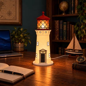 May include: A lighthouse-shaped table lamp with a white conical body, a red roof, and a glowing lantern room. The lamp features black window and door frames, a circular base, and a power cord extending from the back, emitting a warm light.
