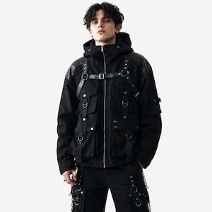 K&ouml;nnte beinhalten: Eine schwarze Kapuzenjacke mit durchgehendem Frontrei&szlig;verschluss, mehreren Utility-Taschen mit silberfarbenen Druckkn&ouml;pfen und einem integrierten Gurtsystem mit verstellbaren Riemen, Metallschnallen und D-Ringen an Brust und Schultern.