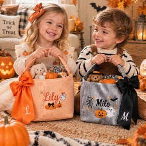 Peut inclure: Deux paniers d'Halloween en tissu avec anses. Le panier rayé orange porte le nom Lily, un fantôme et des citrouilles, avec un nœud orange et la lettre L. Le panier rayé noir et blanc porte le nom Milo, un fantôme et une toile d'araignée.