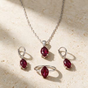 May include: A jewelry set consisting of a silver necklace with a marquise-cut deep red gemstone pendant, a matching silver ring with a marquise-cut red gemstone, and two silver drop earrings featuring marquise-cut red gemstones.