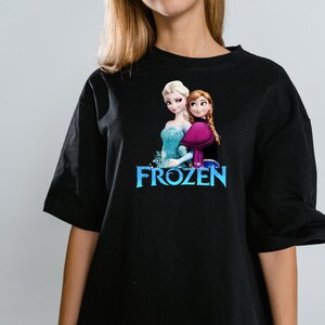 Peut inclure: Un t-shirt noir &agrave; manches courtes avec une impression graphique des personnages Elsa et Anna du film Frozen. Le motif comprend le texte bleu du logo Frozen positionn&eacute; directement sous les deux personnages, qui se tiennent c&ocirc;te &agrave; c&ocirc;te.