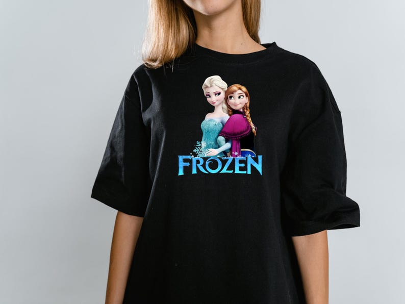 Peut inclure: Un t-shirt noir &agrave; manches courtes avec une impression graphique des personnages Elsa et Anna du film Frozen. Le motif comprend le texte bleu du logo Frozen positionn&eacute; directement sous les deux personnages, qui se tiennent c&ocirc;te &agrave; c&ocirc;te.