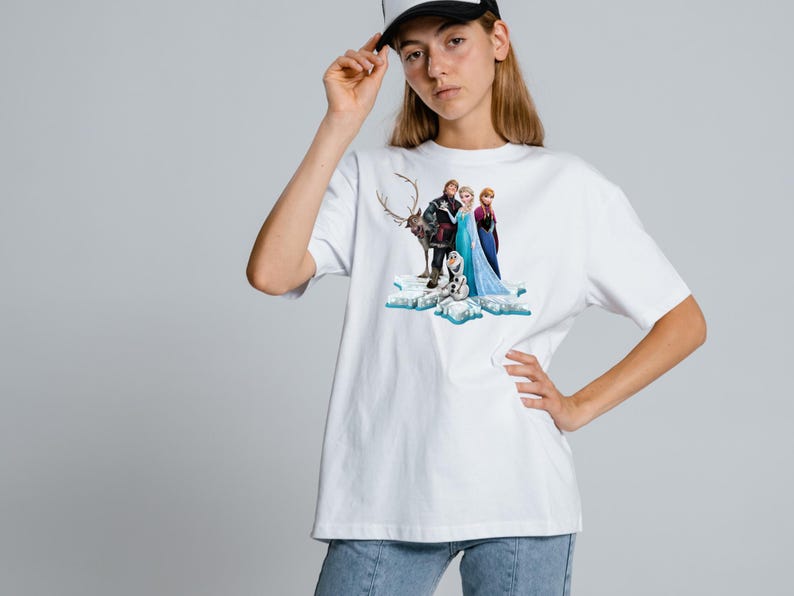 Peut inclure: Un t-shirt blanc &agrave; manches courtes avec une impression graphique des personnages Elsa, Anna, Kristoff, Sven et Olaf de Frozen debout sur une formation de glace bleue et blanche. Le t-shirt a un col rond et une coupe d&eacute;contract&eacute;e.