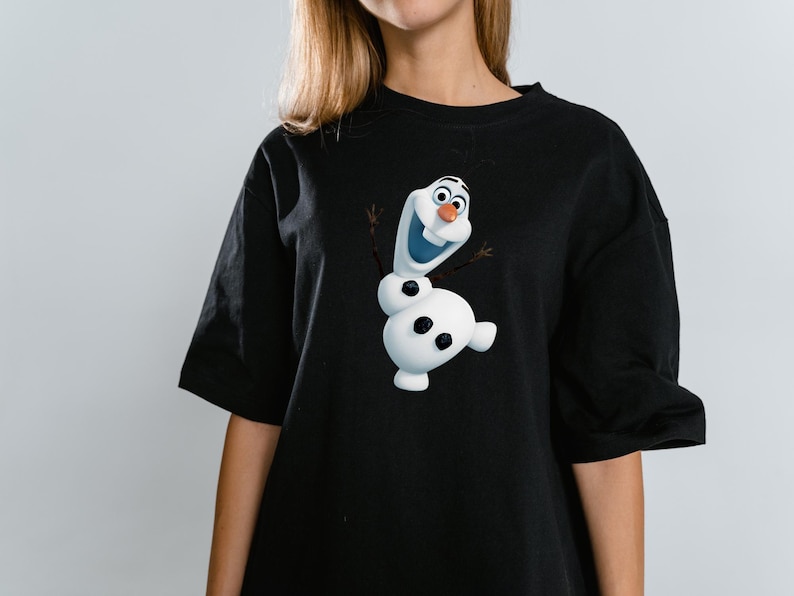 Peut inclure: Un t-shirt noir &agrave; manches courtes avec une impression graphique du bonhomme de neige blanc Olaf du film La Reine des Neiges. Le personnage a un nez en carotte, des bras en brindilles et trois boutons noirs sur le corps, centr&eacute; sur le devant.