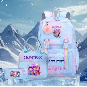 May include: A pastel-colored backpack, lunch bag, and pencil case set featuring a gradient of blue, pink, and purple. The items display the text "HUNTRIX" and "K-POP DEMON HUNTERS" alongside cartoon character illustrations and a fuzzy pink pom-pom.