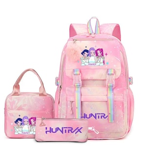 May include: A pink backpack, lunch bag, and pencil case set featuring a repeating anime-style graphic of three characters and the text HUNTR/X. The items have rainbow-striped straps, pink zippers, and a fluffy pink pom-pom attached to the backpack.
