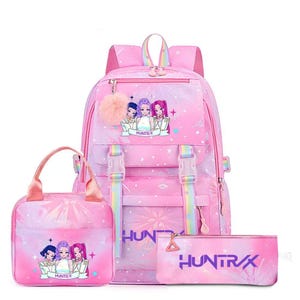 May include: A pink backpack, lunch bag, and pencil case set featuring a repeating star pattern and a graphic of three anime-style characters. The backpack includes rainbow-striped straps, two front buckles, and a fluffy pink pom-pom keychain.