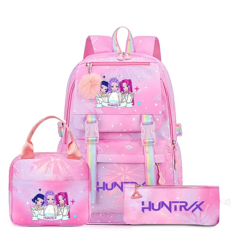 May include: A pink backpack, lunch bag, and pencil case set featuring a repeating star pattern and a graphic of three anime-style characters. The backpack includes rainbow-striped straps, two front buckles, and a fluffy pink pom-pom keychain.
