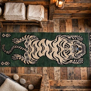 Könnte beinhalten: Ein rechteckiger Teppich mit einer großen, stilisierten Tigerillustration in Beige und Schwarz auf dunkelgrünem Grund. Der Teppich hat ein geometrisches Bordürenmuster und cremefarbene Fransen an beiden Enden und liegt auf einem Holzboden.
