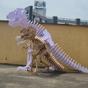 Peut inclure: Deux grands modèles de squelettes de dinosaures construits à partir de panneaux plats emboîtables. L'un est violet clair et le plus petit devant est de couleur beige naturel. Tous deux présentent des cages thoraciques et des dents acérées.