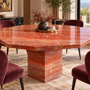 May include: An octagonal dining table crafted from polished red travertine stone with a thick central pedestal base. The table surface features natural stone veining and is topped with a circular tray holding a dark vase and small bowl.