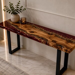 May include: A rectangular console table featuring a natural live-edge wood slab center with prominent knots and grain, flanked by deep red translucent resin edges embedded with small stones. The table is supported by two black metal U-shaped legs.